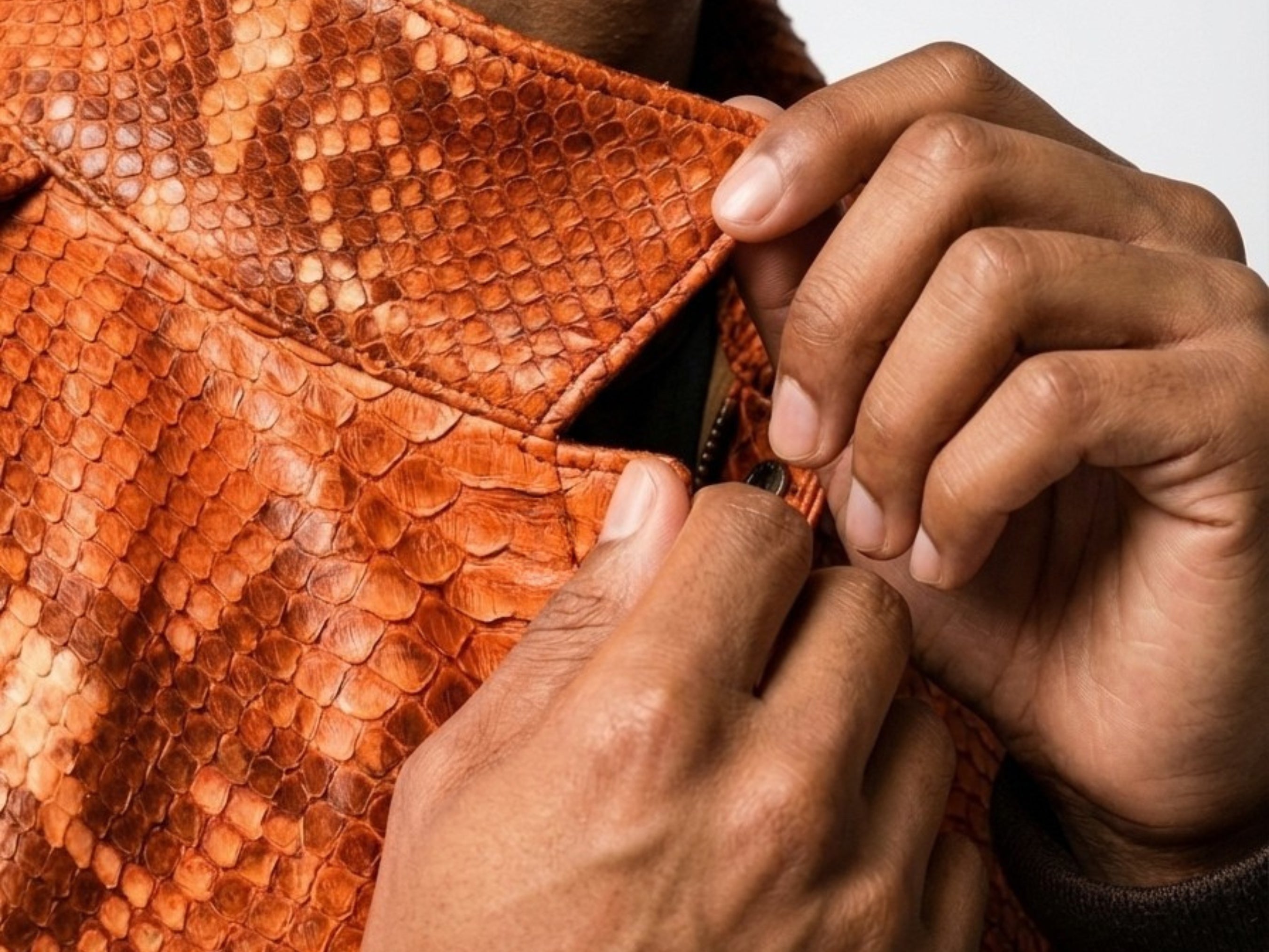 Orange python snakeskin bomber jacket close-up, hands adjusting button placket