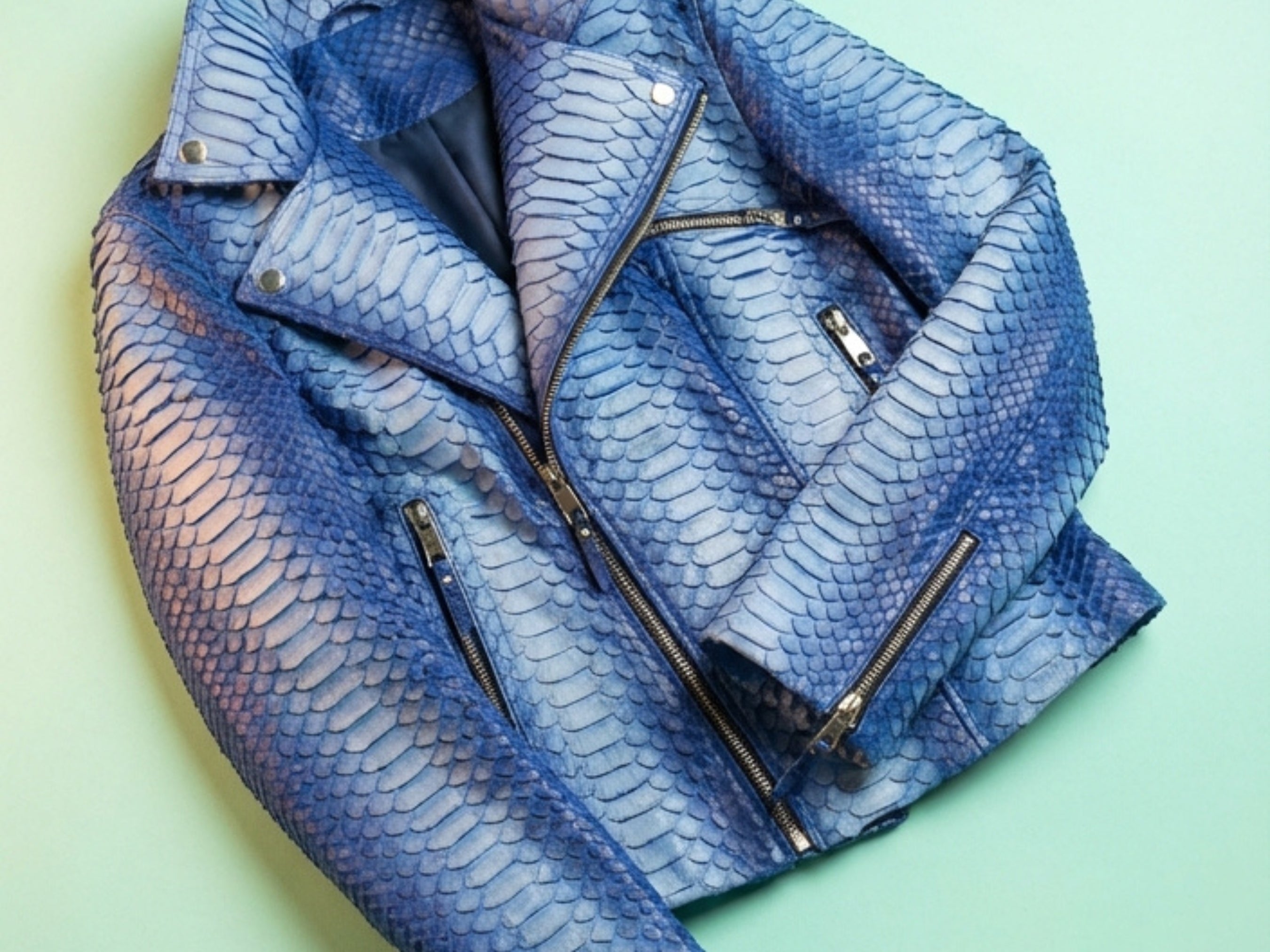 Close-up of blue snakeskin-effect biker jacket with asym zipper, lapels, and metal snap buttons.
